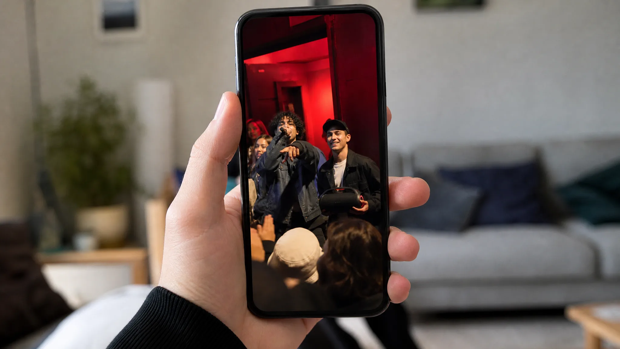 The Freestyle on Your Phone A hand holds an upright phone in a living room, the screen playing a red-lit freestyle with a speaker in view