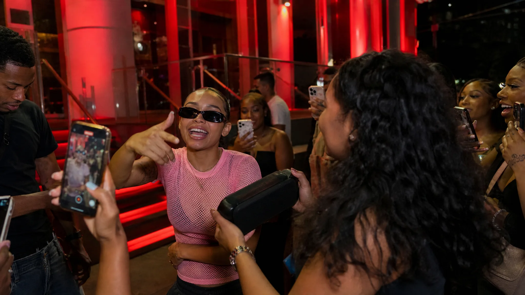 Freestyle at the Red Steps A rapper in a pink mesh tee and black shades gestures at a phone camera as a friend lifts a speaker by red-lit steps